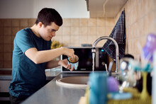 Man With Down Syndrome Washing Dishes In The Kitchen.