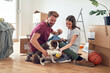 © luckybusiness - cute young adult couple playing with their dog in new apartment with unpacked cardboard boxes around them