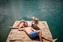 Couple Sunbathing On Wooden Jetty By Lake. Vacation And Adventure In Nature. Hiking, Lifestyle, Nature Concept