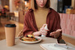 © Mediaphotos - Young woman sitting in modern cafe using hand sanitizer before eating her tasty meal, medium section shot