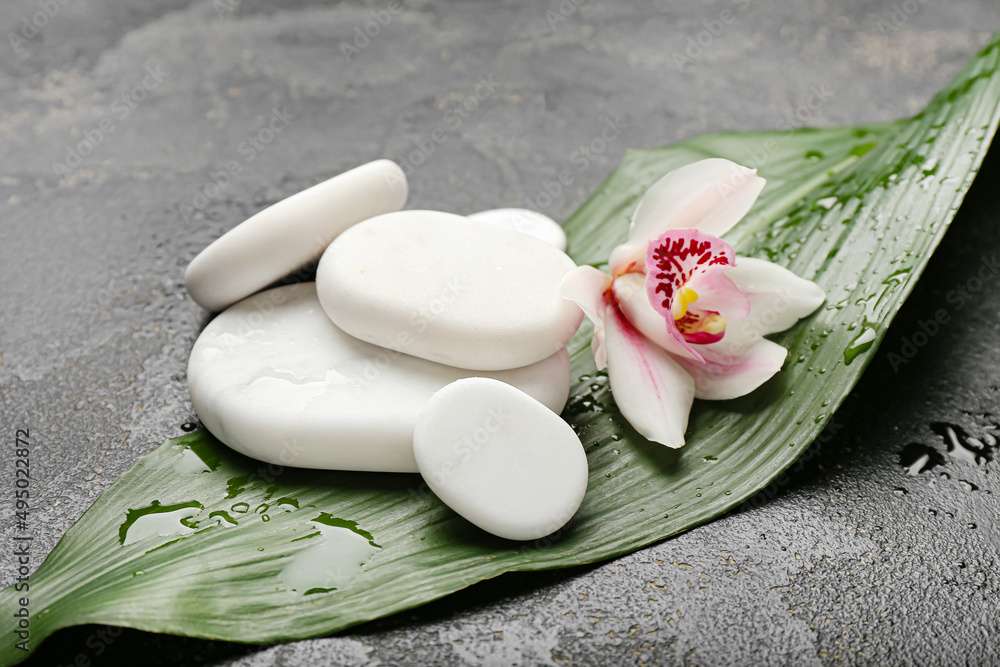 Spa stones with orchid flower and tropical leaf on dark background