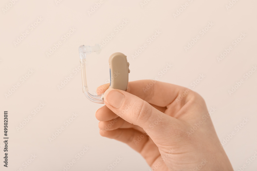 Female hand with hearing aid on light background