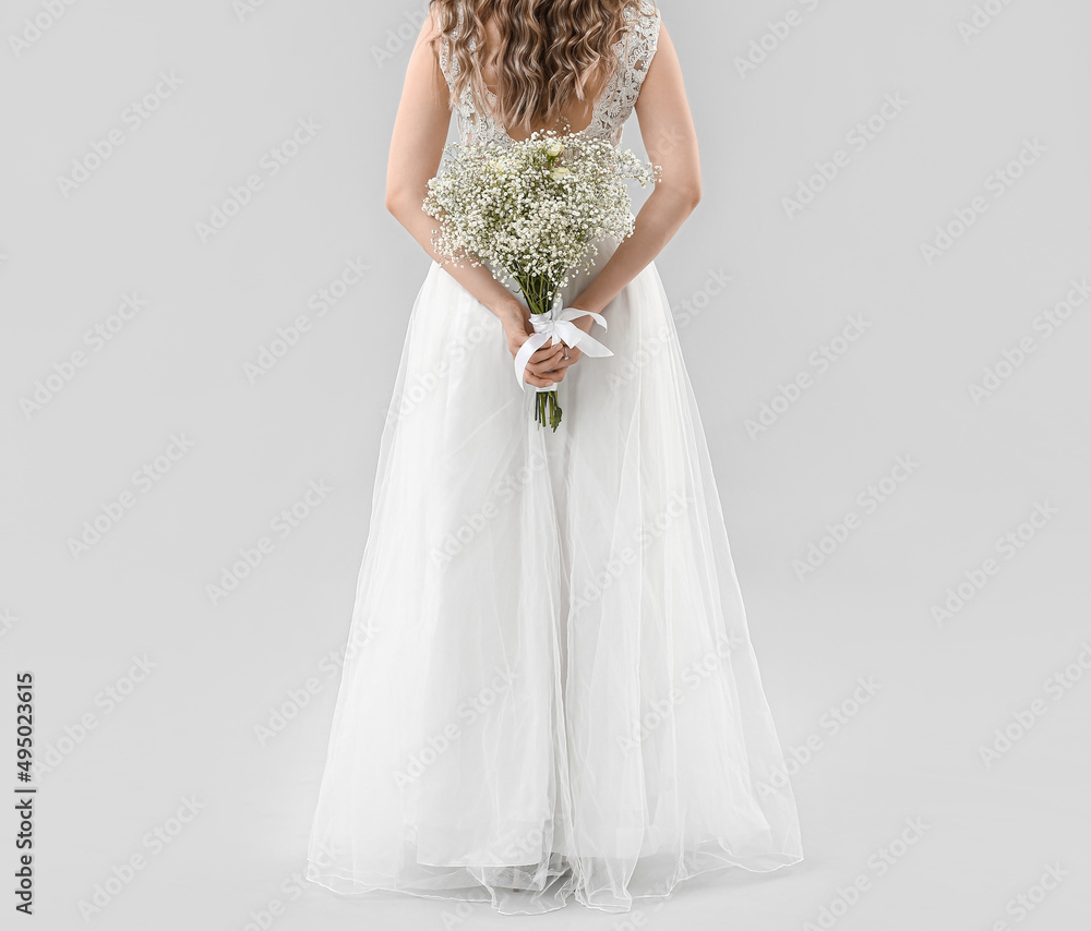 Beautiful bride with bouquet of flowers on light background