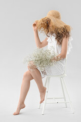 Wall Mural - Pretty young woman with bouquet of flowers sitting on chair against light background