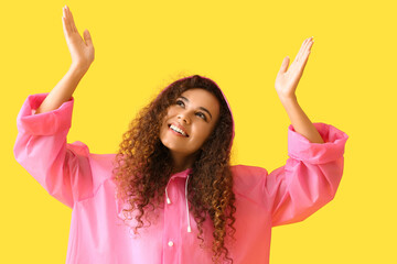 Poster - Smiling young African-American woman in pink raincoat on yellow background