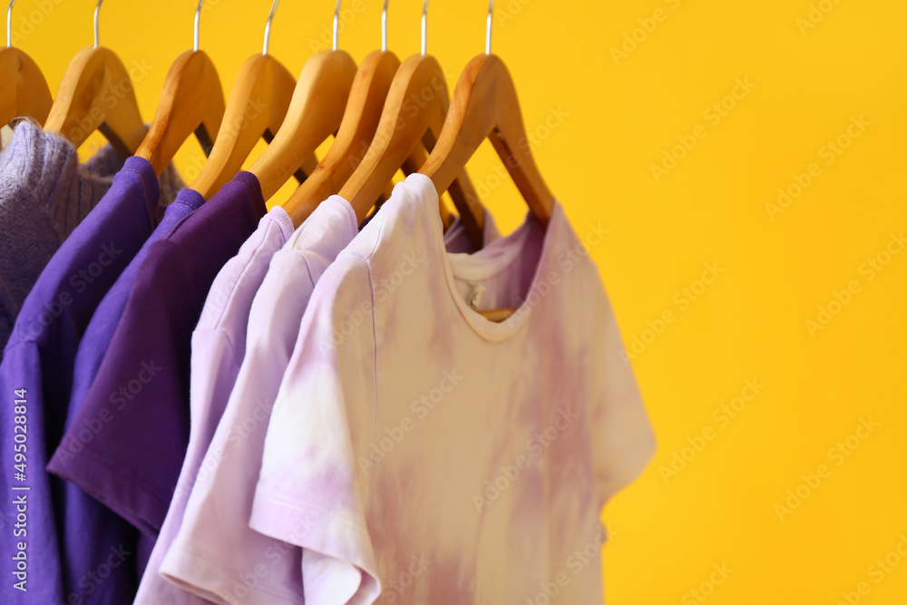 Clothes in purple shades hanging on yellow background, closeup