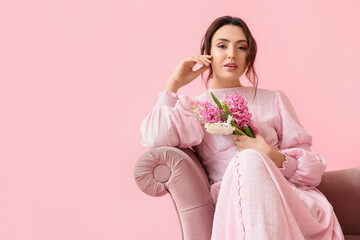 Sticker - Pretty young woman with hyacinth flowers sitting on sofa against pink background