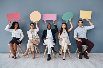 Poster - Its a hot topic in the business world right now. Portrait of a group of businesspeople holding speech bubbles while sitting in line against a grey background.