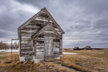 The Exterior Of An Abandoned Schoolhouse With  Two Abandoned Homes In The Background On The Prairies Near Battrum, Saskatchewan