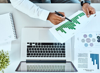 Wall Mural - What does your business data say. High angle shot of an unrecognizable businessman going through paperwork while working on a laptop in an office.