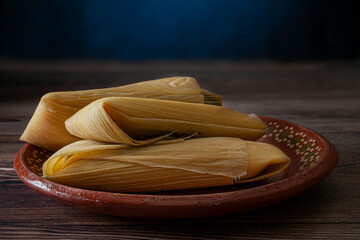 Tamales de elote or corn tamales on a Mexican clay plate over a wooden rustic table and a dark blue background. Macro photography