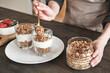 © Mediaphotos - Close-up of unrecognizable woman standing at kitchen counter and putting muesli into mug while preparing granola for breakfast