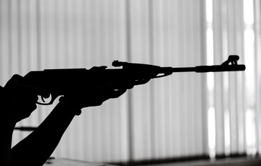 Silhouette of a gun in the hands against the background of a window