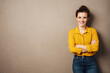 © contrastwerkstatt - young smiling business woman with yellow blouse stands in front of brown background