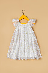 Wall Mural - White baby dress with flowers on a hanger on a beige background. Fashion kids outfit for summer.