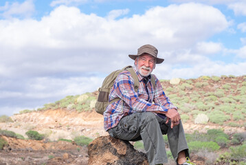 portrait of a senior bearded man carrying a backpack while resting looking at the mountain and smili
