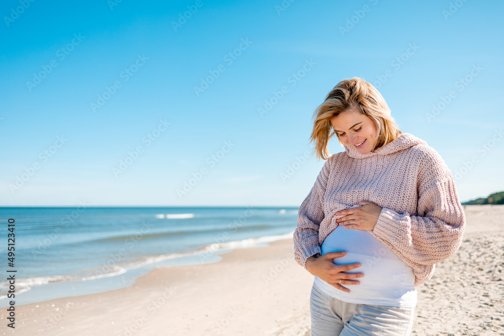 Happy beautiful pregnant woman walking on sandy beach