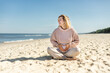 © leszekglasner - Pregnant woman in sweater sitting on seashore and relaxing