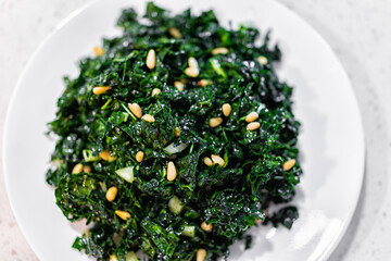 Flat top closeup texture view of green kale vegan vegetarian salad on white plate with pine nuts and olive oil background