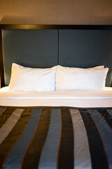 Poster - Bedroom room at night with white pillows and sheets on mattress made bed front view in modern hotel motel room with nobody and stylish decor vertical view