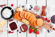 Breakfast or brunch pancake buffet table scene. Mini pancakes with a variety of toppings. Above view over a white wood background.