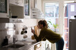 © Zamrznuti tonovi - Woman standing in the kitchen and drinking cup of tea while using smartphone