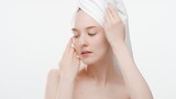 Fototapeta Zachód słońca - Beauty portrait of young ginger woman with towel on her head who touches her face with both hands on white background