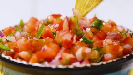 Wall Mural - Pico de Gallo close up. Hand dipping tortilla chip into plate of traditional pico de gallo. Bowl of tasty Pico de Gallo salsa and nachos chips. Mexican food concept