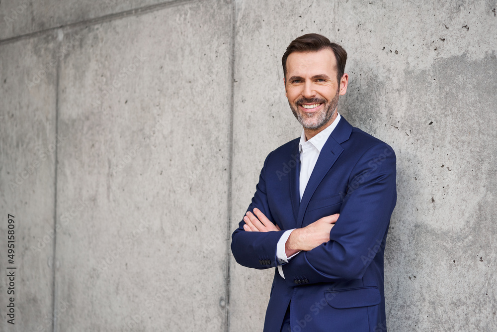 Portrait of smiling successful businessman in suit standing against ...