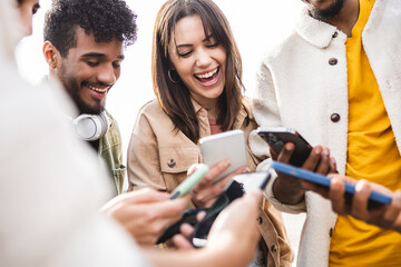 Young group of people using mobile phone outdoors - Addicted diverse friends holding smartphones sharing social media content on digital network app - Youth and technology concept