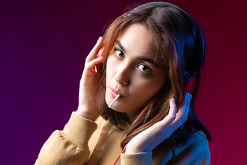 Wall Mural - Young beautiful fashionable hipster girl dressed in a hoodie  listening to music in red headphones in a studio red dramatic background