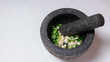 A mortar and pestle filled with fresh garlic, coriander, black peppercorns and salt to prepare a thai curry paste.
