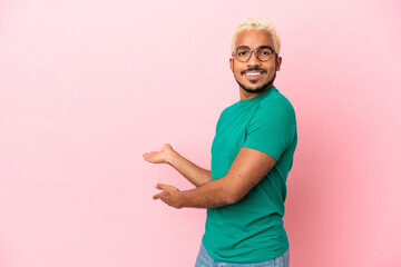 Wall Mural - Young Colombian handsome man isolated on pink background extending hands to the side for inviting to come