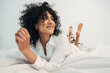 © Daniel - Smiling happy young mixed race woman lying on bed relaxing at home.