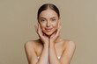 © VK Studio - Refreshed young woman touches face gently has clean healthy skin wears minimal makeup wrapped in bath towel