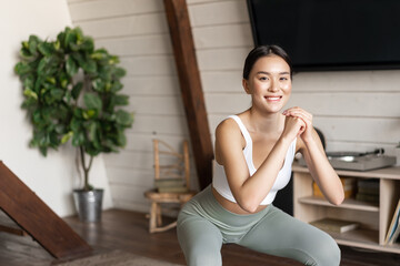 Wall Mural - Young asian fitness woman with healthy fit body, doing squats, morning workout, wearing activewear, standing at home in living room and having training session