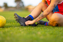 Female Footballer Sitting On Grass Adjusting Boot