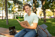 © Prostock-studio - Happy student guy reading interesting book, having rest after classes, sitting on bench in parkland on sunny day