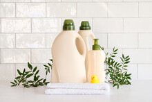 Eco Friendly Organic Natural Baby Laundry Detergent Container And Soap Gel Bottle With Branch Of Green Leaves, Towel And Yellow Duck On Table In Bathroom.