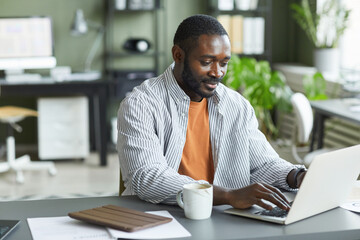 Portrait of adult black man working at home office and using laptop, copy space