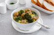 © Iryna - Broccoli and meatball soup. White bowl of homemade soup with mini meatballs, broccoli, potato, carrot and fresh herbs in clear broth. Light gray background, selective focus.