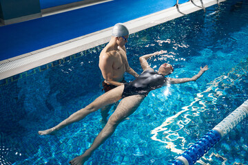 Trainer showing to young woman how to swim