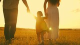 Fototapeta Natura - happy family park. little kid daughter runs across meadow sunset. mother father kid child travel together. childhood dream run and play. family walk sunshine. cheerful child holds mom dad by hand