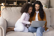 © fizkes - Happy young African mother and gen Z daughter girl watching movie, sitcom, online TV on laptop, using virtual learning app, shopping, making video call, relaxing on home couch together