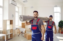 Smiling Young Male Movers Carrying Carpet Unload Goods In Client Home Or Office. Happy Removal Company Male Workers Unpack Help Client With Boxes During Moving Or Relocation. Transportation.