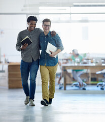 Poster - Colleagues and friends. Shot of a two young coworkers talking together while walking arm in arm through their office.