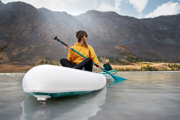 Two young girls walks on stand up paddle boards at mountain lake