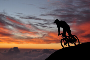 Silhouette of a mountain biker enjoying downhill during the sunset. Cyclist silhouette on the hill beautiful colorful sky and clouds in the background.