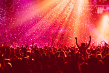 A Crowded Concert Hall With Scene Stage In Red Lights, Rock Show Performance, With People Silhouette, Colourful Confetti Explosion Fired On Dance Floor Air During A Concert Festival