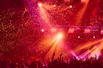 A crowded concert hall with scene stage in red lights, rock show performance, with people silhouette, colourful confetti explosion fired on dance floor air during a concert festival